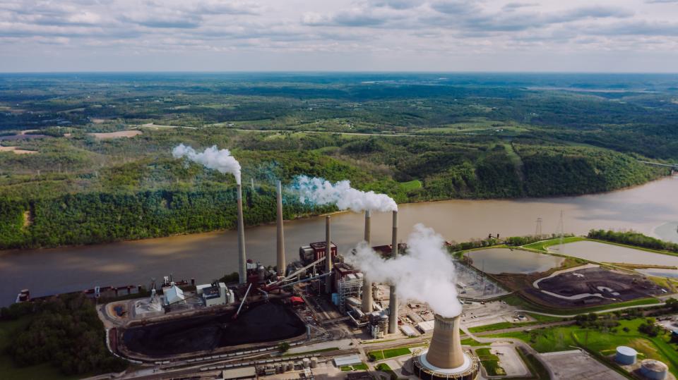 factory with smoke pouring out next to a river