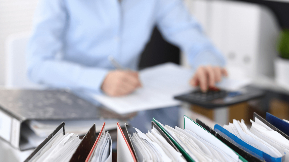 Binders with Male in background writing on documents