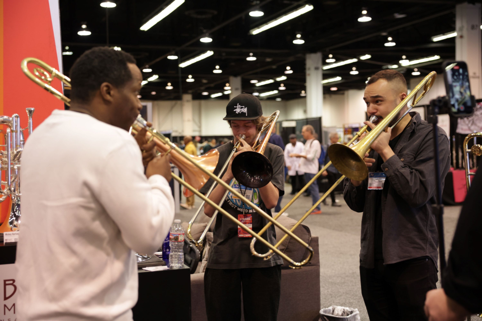 three men play trombones in namm show booth