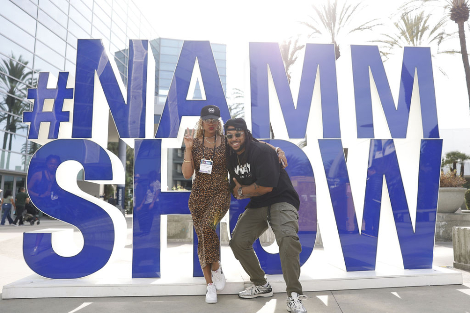 a man and woman pose in front of the hashtag namm show sign